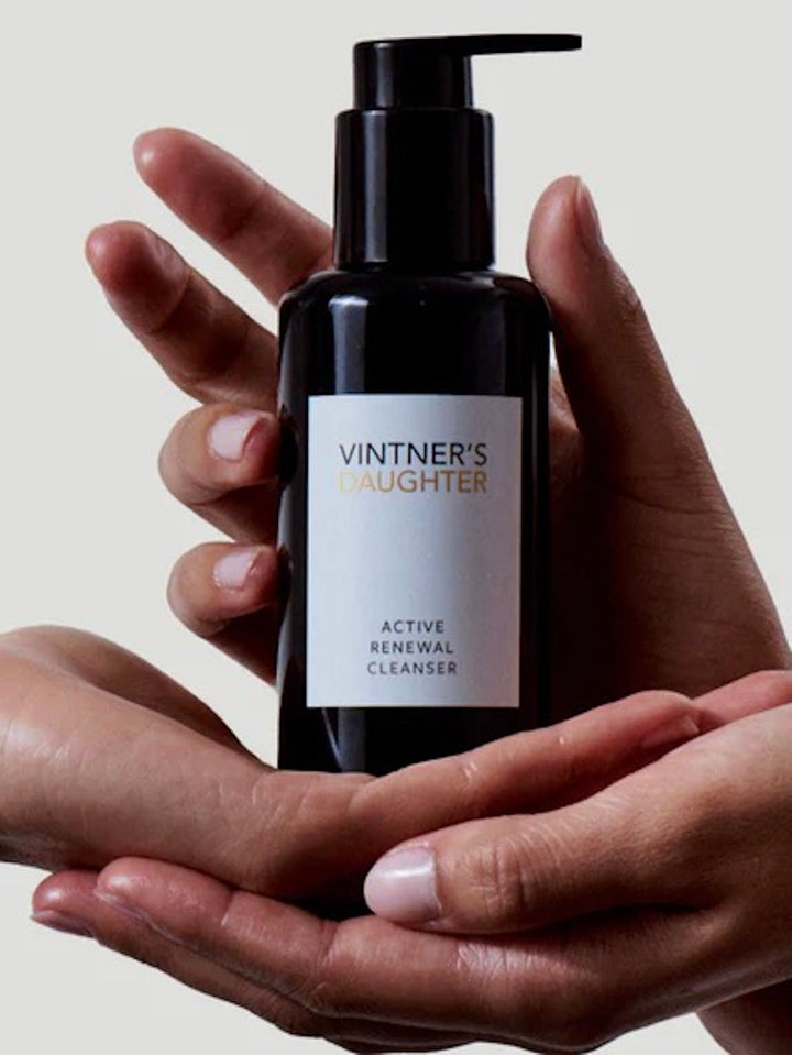 Hand holding a bottle of 'Vintner's Daughter' Active Renewal Cleanser against a neutral background