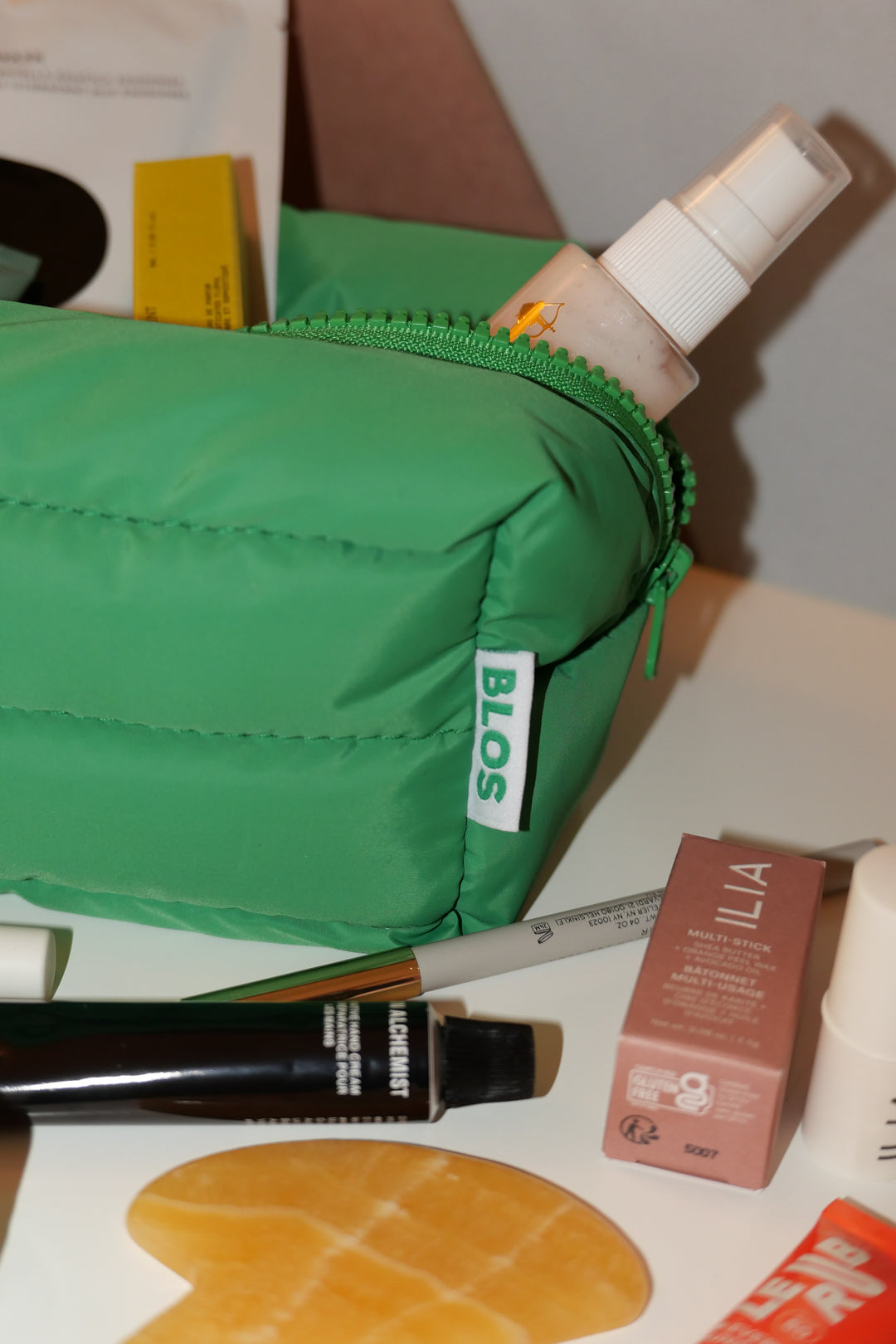 Green blos makeup bag with cosmetic items on a surface