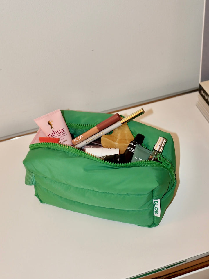 Green makeup bag with cosmetic items on a white surface