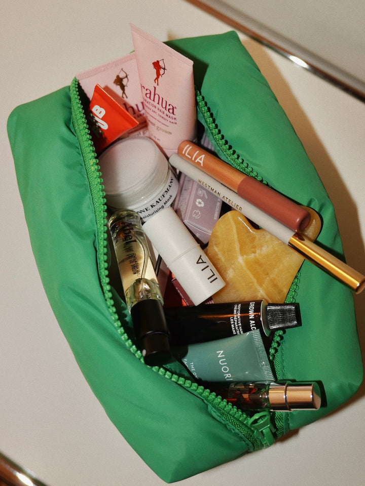 Green makeup bag with various cosmetic products on a white surface