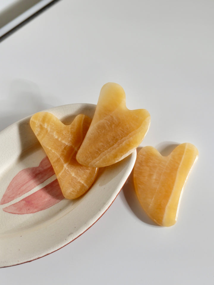 Three yellow jade gua sha  on a white plate with pink floral design.
