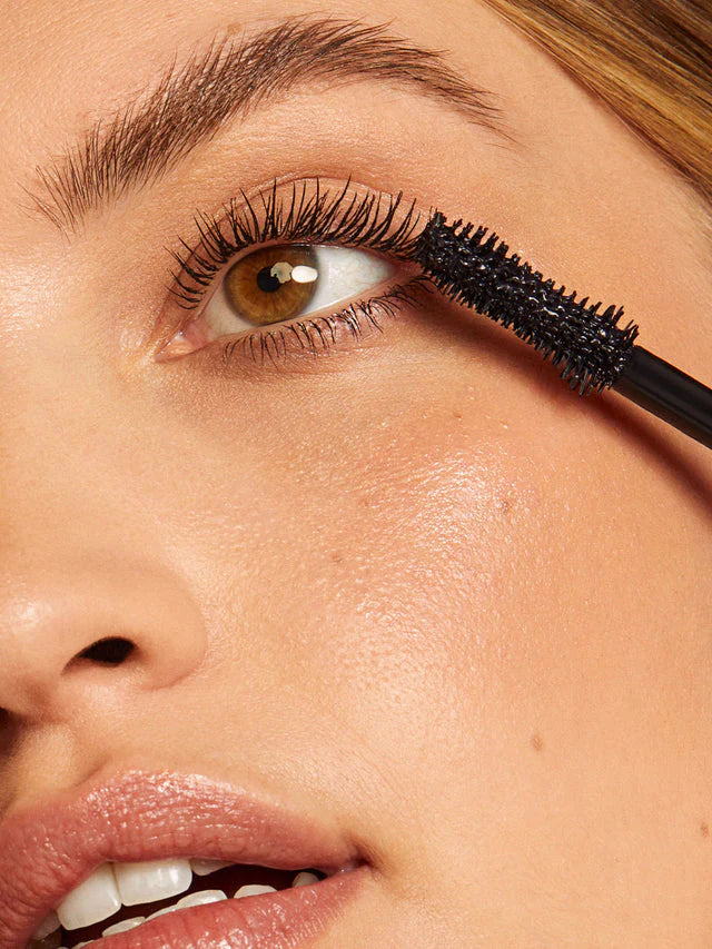 Close-up of a person applying mascara to their eyelashes with a brush.