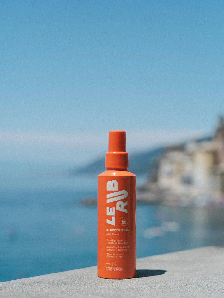 Orange bottle labeled Le RUB on a stone ledge with a blurred coastal background