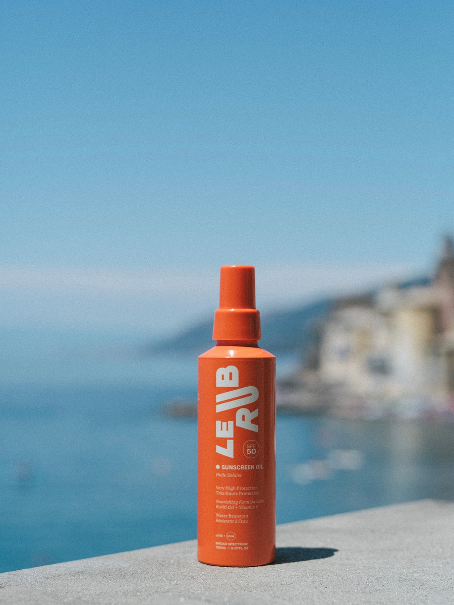 Orange bottle labeled Le RUB on a stone ledge with a blurred coastal background
