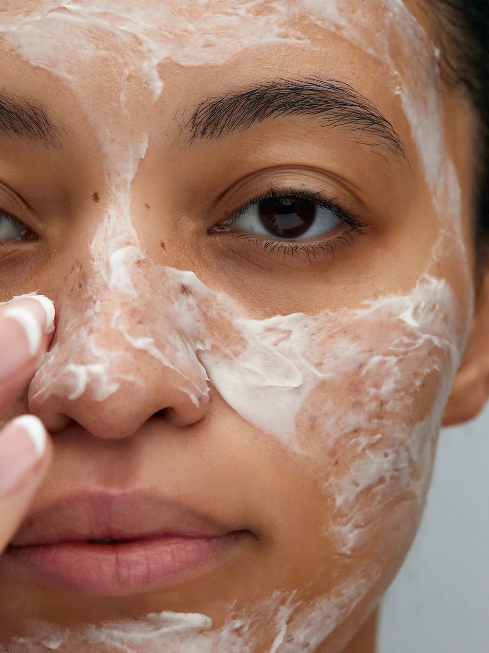 Close-up of a person applying a facial mask with a neutral background
