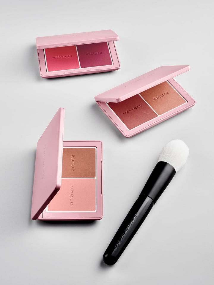 Makeup product set with pink cases and a brush on a light gray background
