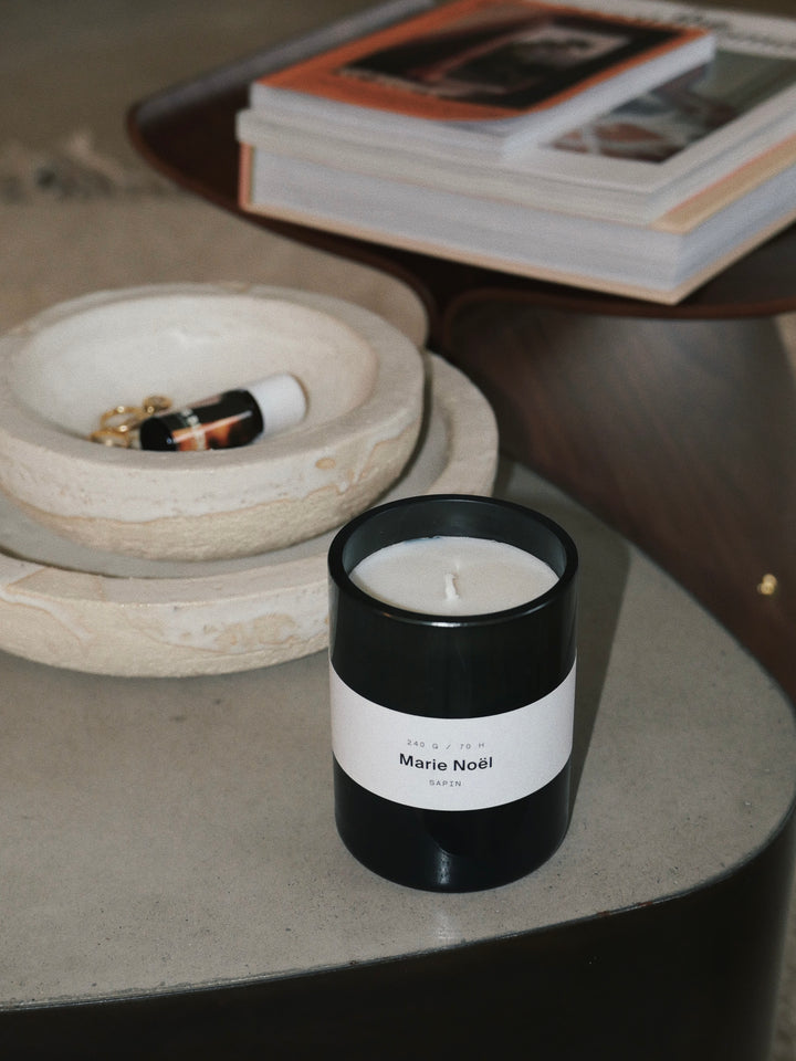 Candle labeled 'Marie Noël' on a table with a bowl and books in the background