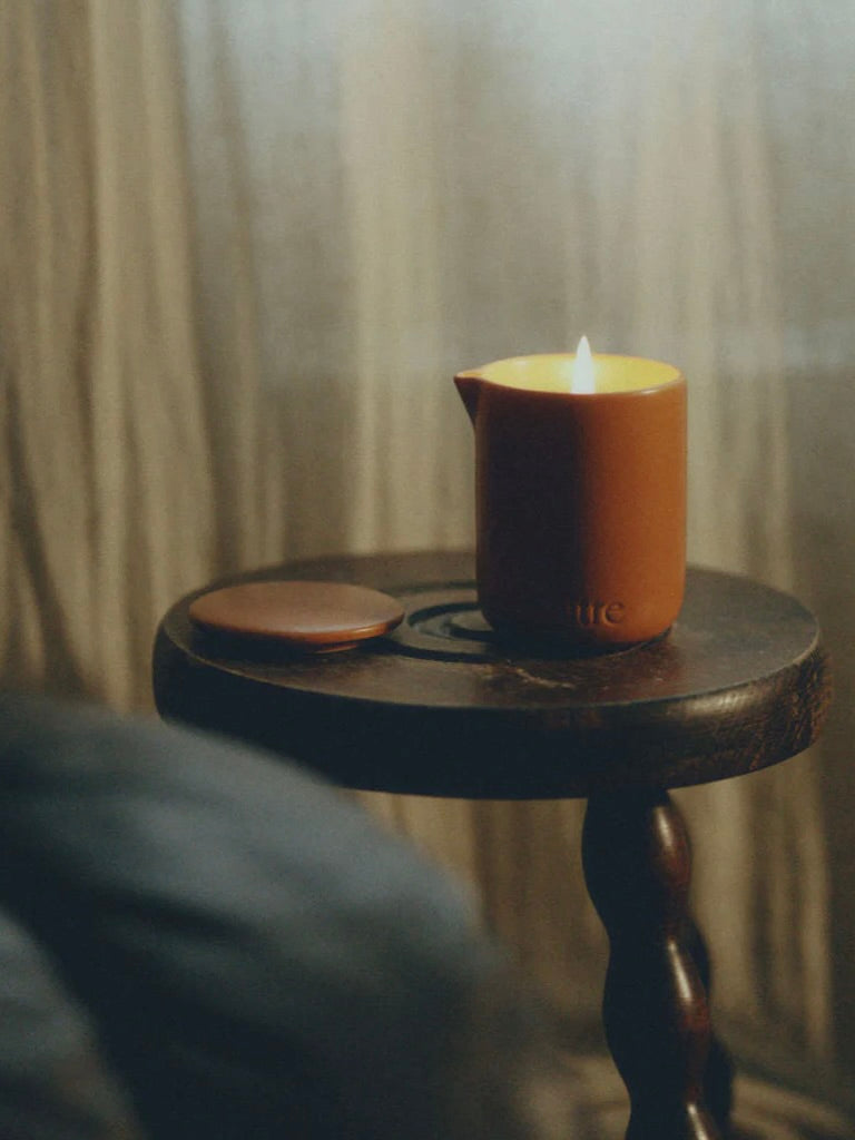 Candle in a terracotta holder on a wooden table with a blurred background