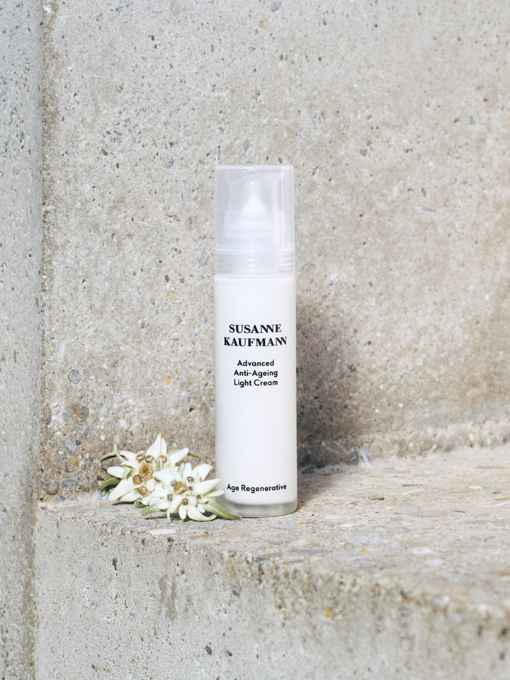 Skincare bottle labeled 'Susanne Kaufman' on a stone surface with flowers.