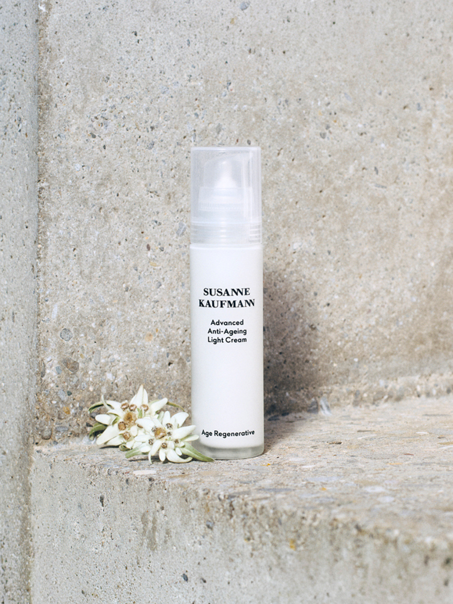 Skincare bottle labeled 'Susanne Kaufman' on a stone surface with flowers.