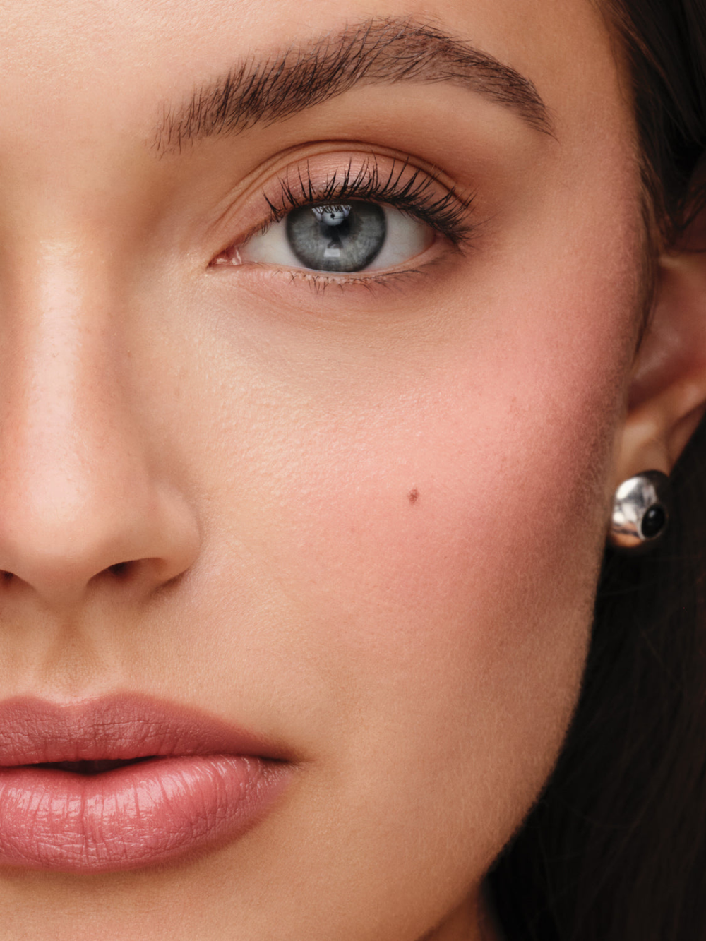 Close-up of a woman's face showing a small silver and black round stud earring on her earlobe.