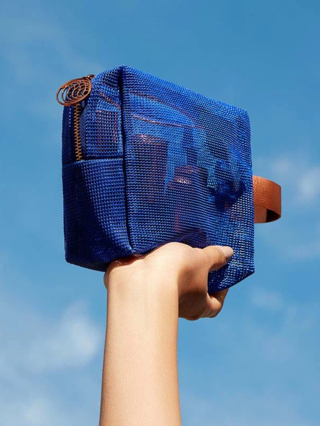 Hand holding a blue mesh bag against a clear blue sky