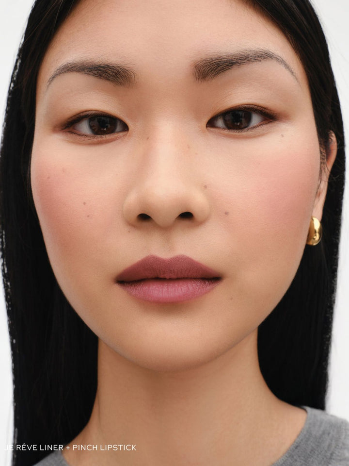 Close-up of a person with dark hair and a neutral expression on a white background 