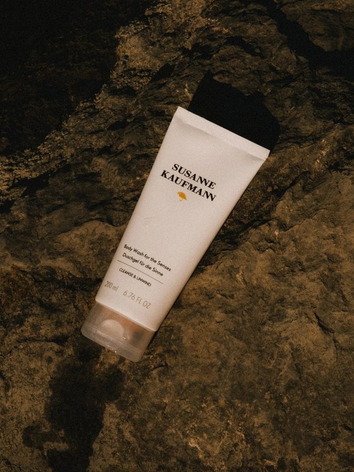 A white tube of Susanne Kauffmann body wash for the sensitive skin, lying diagonally on a dark, textured rock surface.