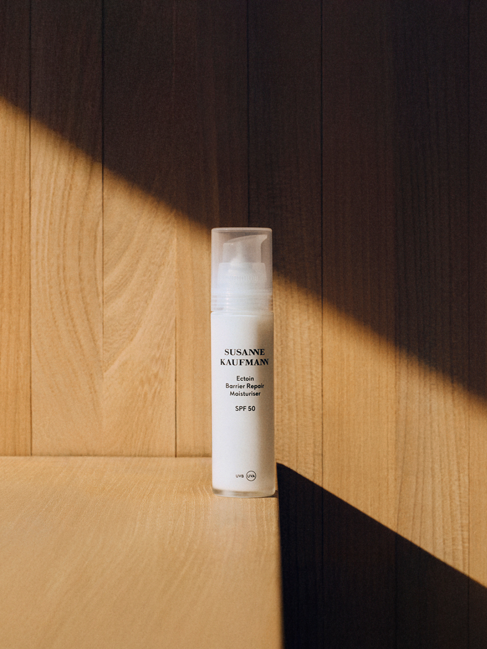 Skincare bottle labeled 'Susanne Kaufmann' on a wooden surface with a shadow effect. Ection barrier repair moisturiser