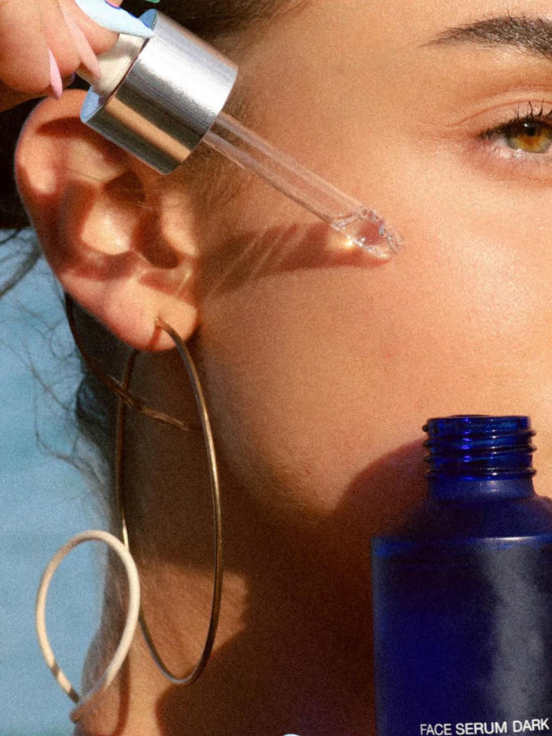 Person applying face serum with a dropper bottle.