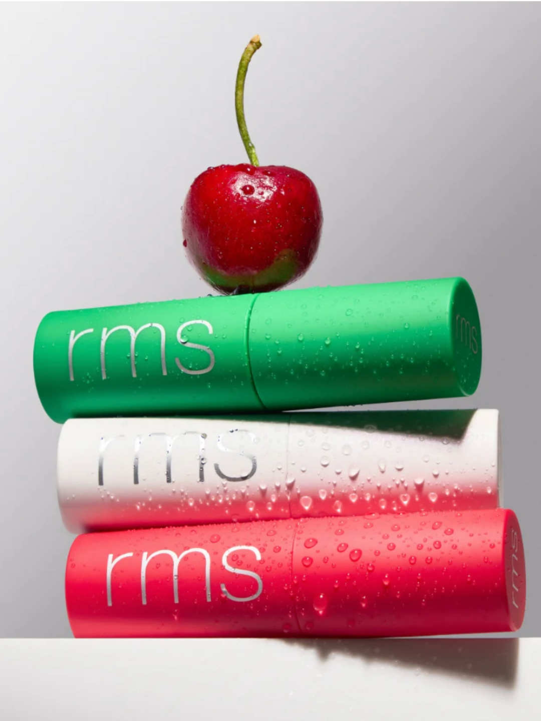 Three RMS beauty products stacked with a cherry on top against a light background