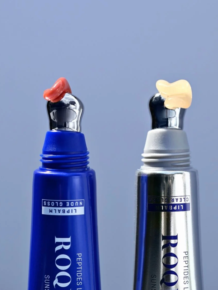 Two lip gloss products with unique applicators on a blue background