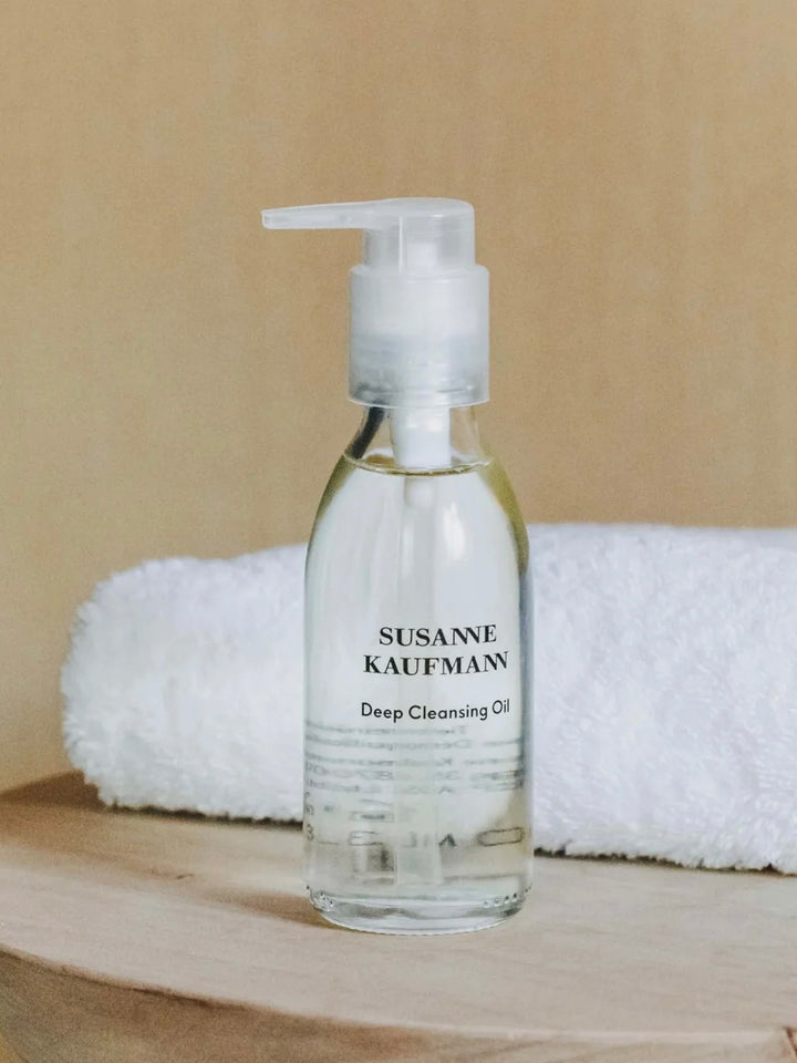 Bottle of Susanne Kaufman Deep Cleansing Oil on a wooden surface with a beige background