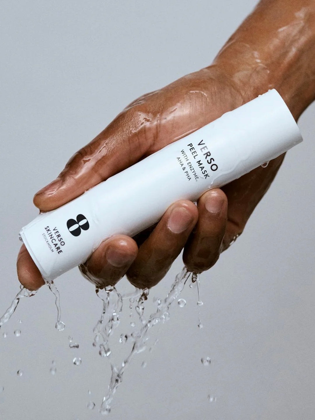Hand holding a white Verso skincare product with water being sprayed. Verso Peel Mask.